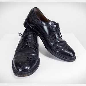 Op de afbeelding: Twee zwarte leren brogueschoenen met vetersluiting. De schoenen hebben een wingtip-ontwerp en zijn gepolijst.