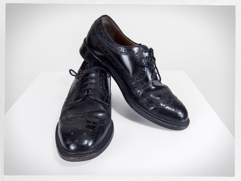 Op de afbeelding: Twee zwarte leren brogueschoenen met vetersluiting. De schoenen hebben een wingtip-ontwerp en zijn gepolijst.