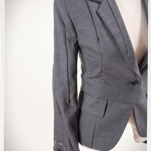 May include: A gray blazer with a single button closure and a pocket on the front. The blazer has a fitted silhouette and a textured fabric.