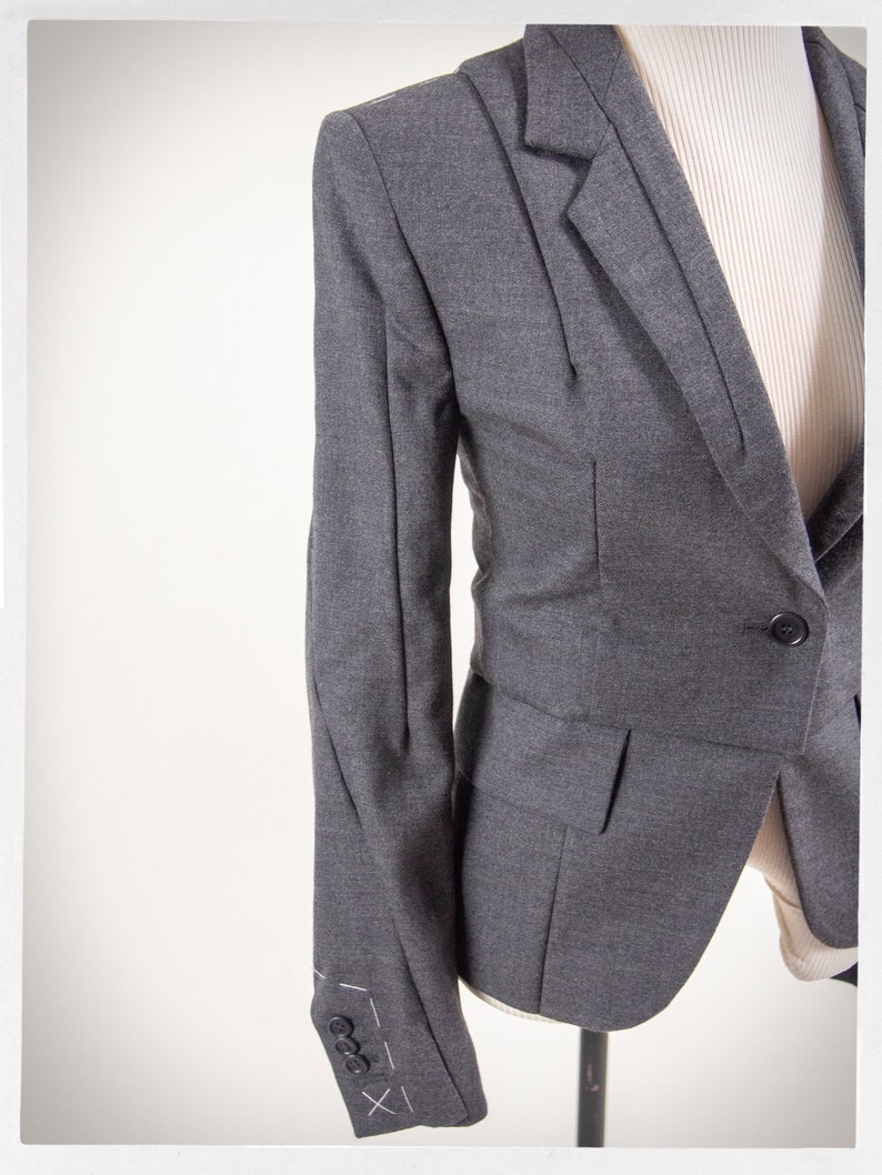May include: A gray blazer with a single button closure and a pocket on the front. The blazer has a fitted silhouette and a textured fabric.