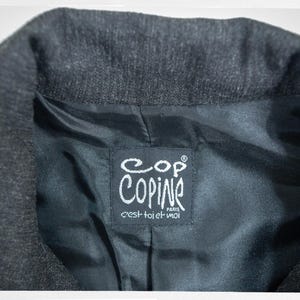 May include: Close-up of a dark gray blazer collar with a black satin lining. The lining features a white label with the brand name "Copine Paris" and the phrase "c'est toi et moi".
