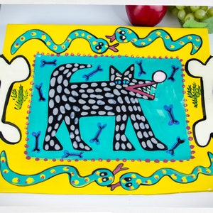 May include: A yellow ceramic serving platter with a black and white spotted dog illustration in the center. The dog is surrounded by blue bones and two green snakes with yellow spots. The platter has a yellow border with a red and white polka dot pattern.