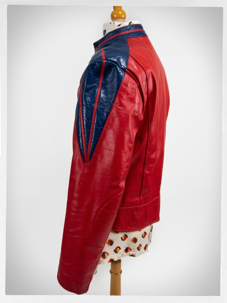 May include: A red leather jacket with blue leather panels on the shoulders and sleeves. The jacket has a stand-up collar and a zipper closure.