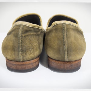 Puede incluir: Un par de mocasines de ante marr&oacute;n con ribete de cuero marr&oacute;n claro. Los mocasines tienen un aspecto desgastado y est&aacute;n ligeramente deste&ntilde;idos.