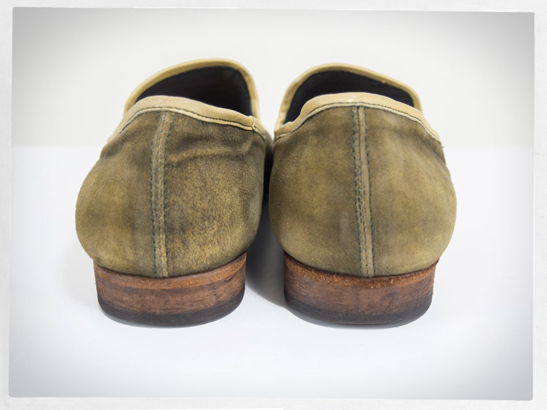 Puede incluir: Un par de mocasines de ante marr&oacute;n con ribete de cuero marr&oacute;n claro. Los mocasines tienen un aspecto desgastado y est&aacute;n ligeramente deste&ntilde;idos.
