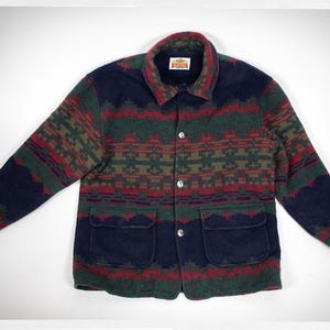 May include: A navy blue jacket featuring a multi-coloured geometric pattern in red, green, and tan. The jacket has a fold-down collar, a front button closure with three silver-toned buttons, and two large patch pockets. A Kanata label is at the neck.