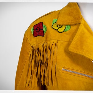 May include: A yellow suede jacket with beaded flower embellishments on the shoulder. The jacket has fringe along the sleeves and a zipper closure.