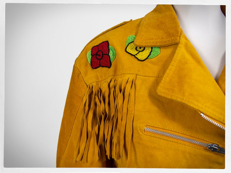 May include: A yellow suede jacket with beaded flower embellishments on the shoulder. The jacket has fringe along the sleeves and a zipper closure.