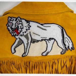 May include: A yellow suede jacket with a beaded wolf design on the back. The jacket has fringe along the bottom.