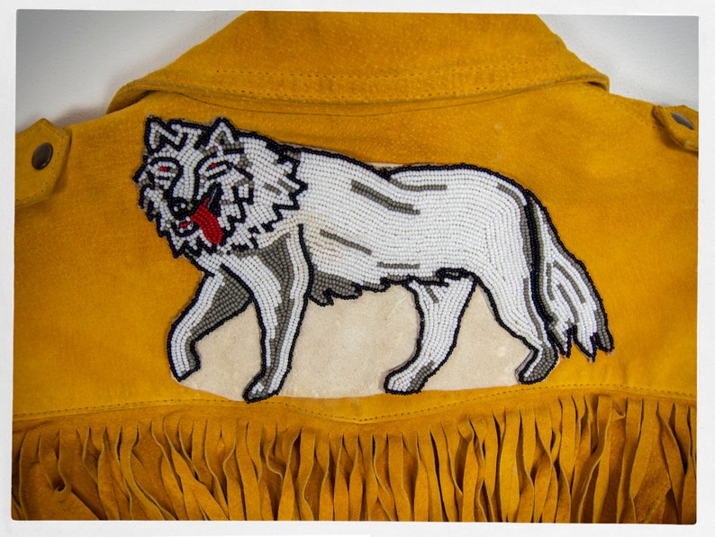 May include: A yellow suede jacket with a beaded wolf design on the back. The jacket has fringe along the bottom.