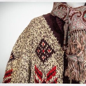May include: A brown, cream, and red knitted cardigan with a paisley patterned scarf. The cardigan has a geometric pattern and the scarf has a fringe.
