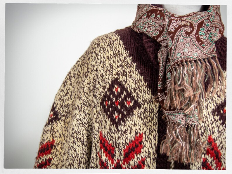 May include: A brown, cream, and red knitted cardigan with a paisley patterned scarf. The cardigan has a geometric pattern and the scarf has a fringe.