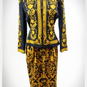 Puede incluir: Un traje de falda negro y dorado con una chaqueta entallada y una falda con estampado floral. El traje est&aacute; hecho de una tela sedosa y tiene un aspecto vintage.