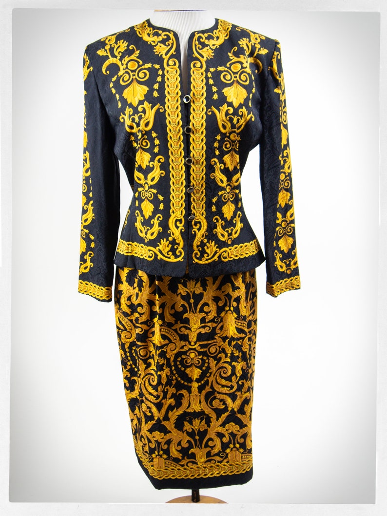 Puede incluir: Un traje de falda negro y dorado con una chaqueta entallada y una falda con estampado floral. El traje est&aacute; hecho de una tela sedosa y tiene un aspecto vintage.