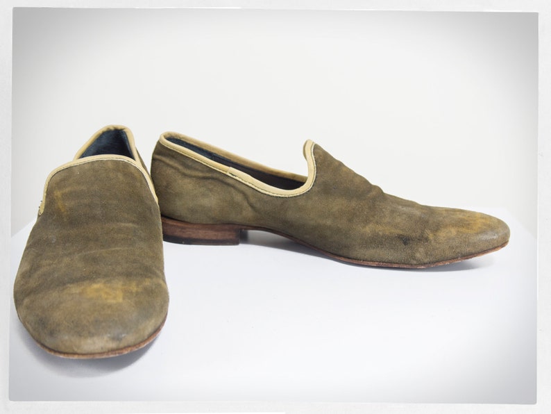 Puede incluir: Un par de mocasines de ante marr&oacute;n con un ribete marr&oacute;n claro alrededor de la parte superior. Los mocasines tienen una punta puntiaguda y un tac&oacute;n bajo.