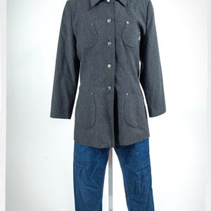May include: A gray button-down jacket with four pockets and silver buttons, paired with blue denim jeans. The jeans have cuffed hems. The jacket is displayed on a mannequin.