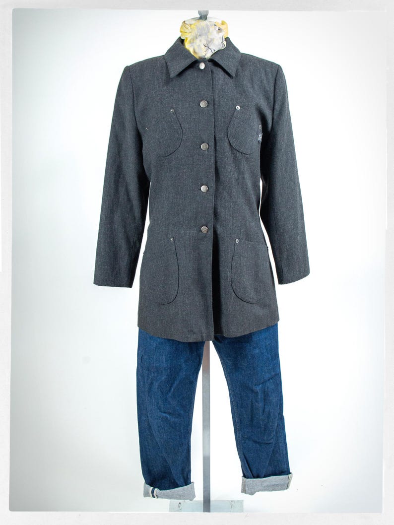 May include: A gray button-down jacket with four pockets and silver buttons, paired with blue denim jeans. The jeans have cuffed hems. The jacket is displayed on a mannequin.