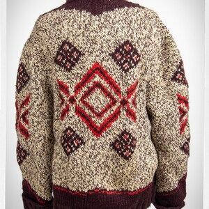 May include: A brown and cream knitted cardigan with a red and brown geometric pattern. The cardigan has a brown collar and a brown band around the bottom.