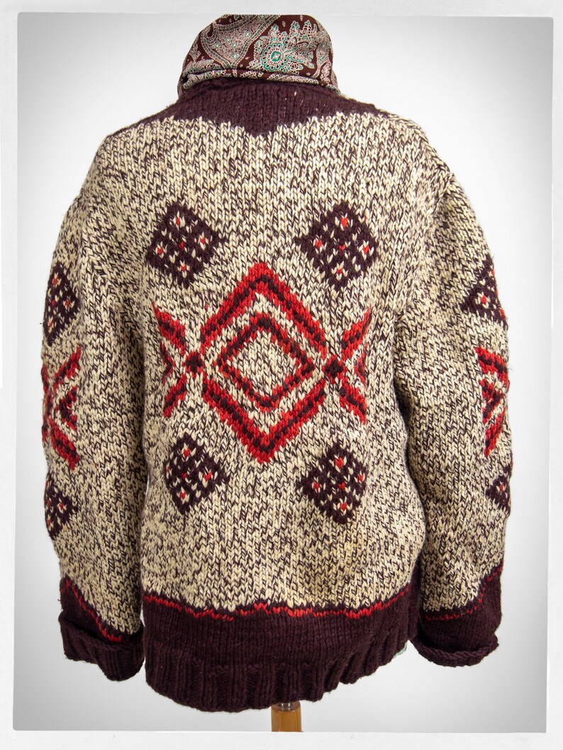 May include: A brown and cream knitted cardigan with a red and brown geometric pattern. The cardigan has a brown collar and a brown band around the bottom.