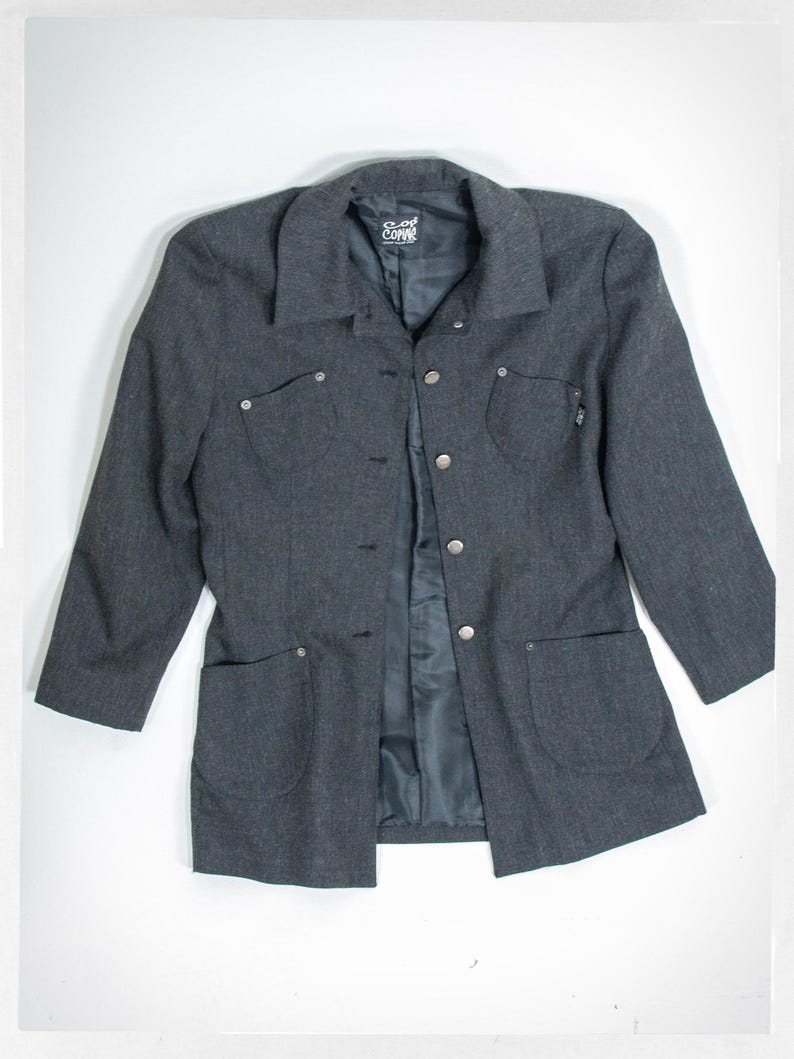 May include: A dark gray blazer with a collared neckline, button closure, and two front pockets. The blazer has long sleeves and a tailored fit. The brand name "Copac" is visible on the label.
