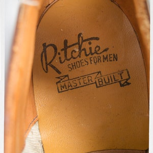 May include: Close-up of the inside of a brown leather shoe with the text "Ritchie Shoes for Men Master Built" printed on the insole.