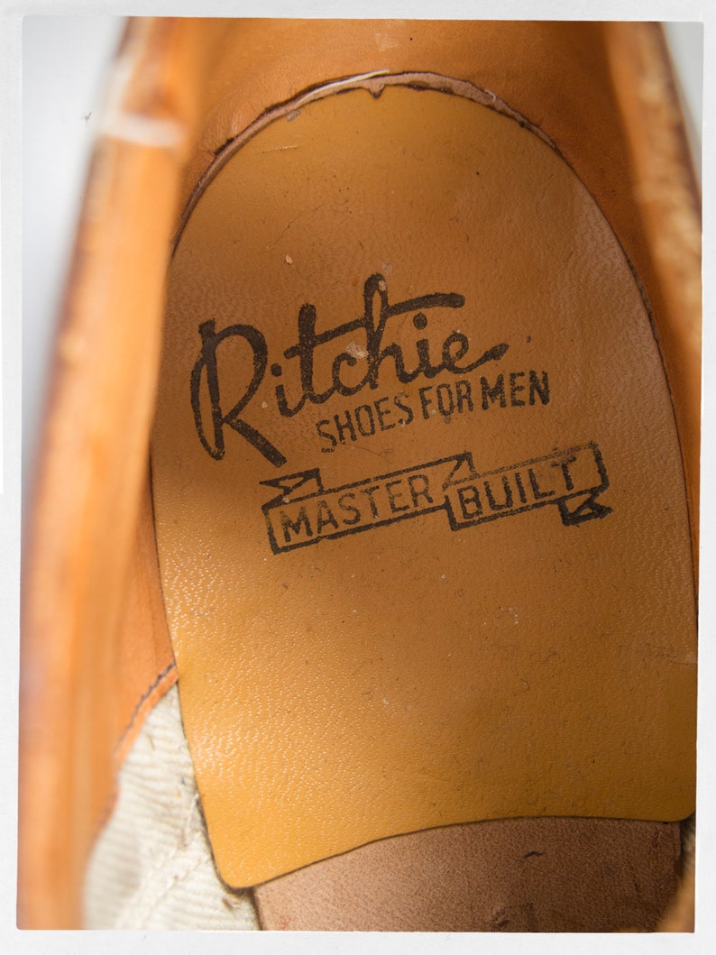 May include: Close-up of the inside of a brown leather shoe with the text "Ritchie Shoes for Men Master Built" printed on the insole.