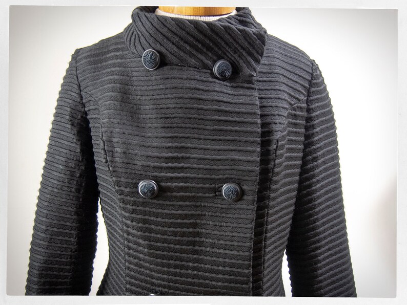 May include: A black ribbed jacket with a high collar and four black buttons. The jacket has a double-breasted closure.