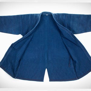 May include: A dark blue denim jacket with a traditional Japanese style, open and laid flat. The jacket is made of a thick, textured fabric and has a simple design.
