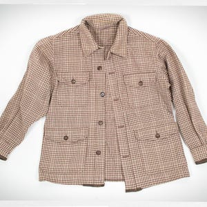 May include: A brown and tan plaid jacket with a collared neckline, four front pockets, and button closures. The jacket has long sleeves with brown trim at the cuffs. The fabric has a classic, vintage look.