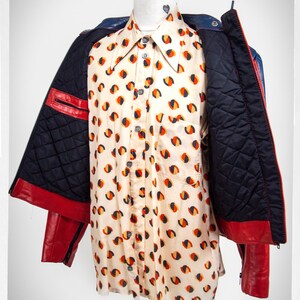 May include: A red and blue leather jacket with a quilted lining. The jacket is open and a white shirt with a geometric pattern is visible underneath.
