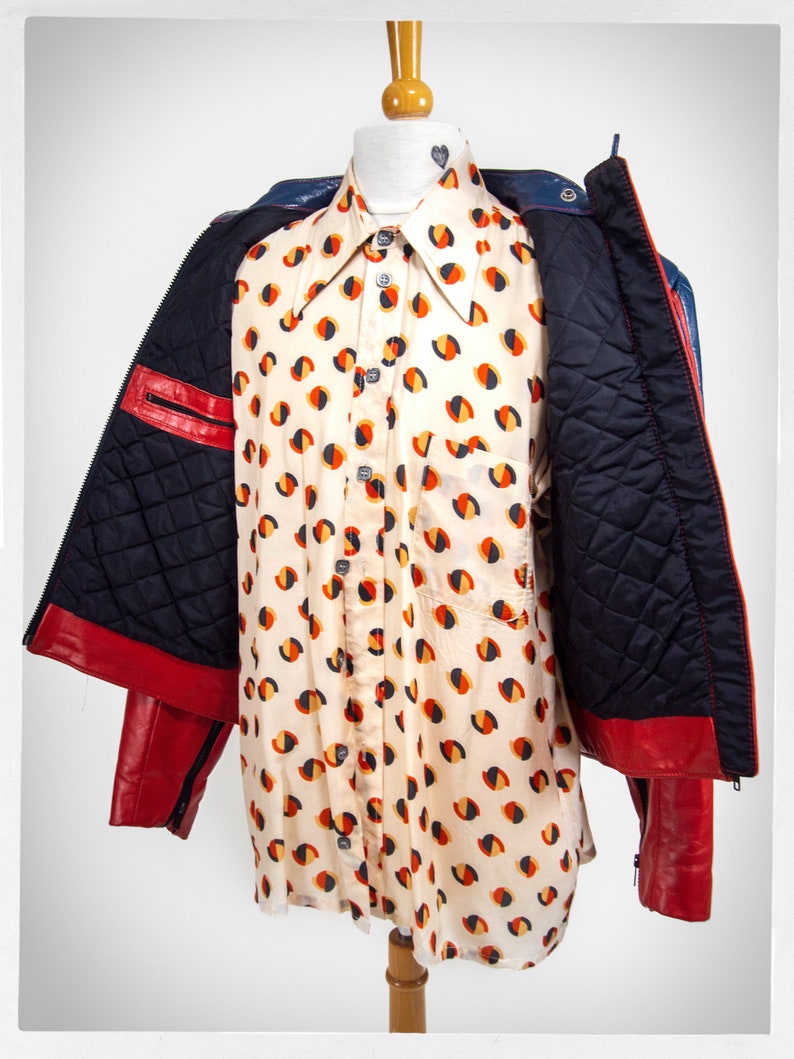 May include: A red and blue leather jacket with a quilted lining. The jacket is open and a white shirt with a geometric pattern is visible underneath.