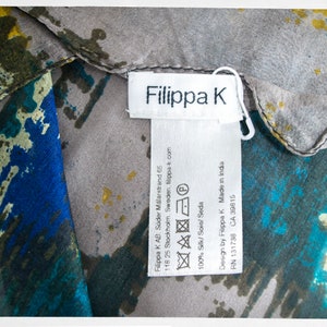 May include: A white tag with black text that reads "Filippa K" and includes care instructions and company information. The tag is attached to a gray and blue patterned fabric.