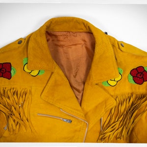 May include: A yellow suede jacket with beaded floral embellishments and fringe detailing. The jacket has a zipper closure and a brown lining.