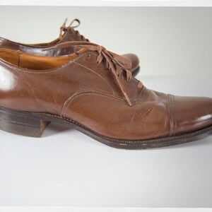 May include: A pair of brown leather lace-up shoes with a cap toe design. The shoes have a polished finish and are made of high-quality leather.