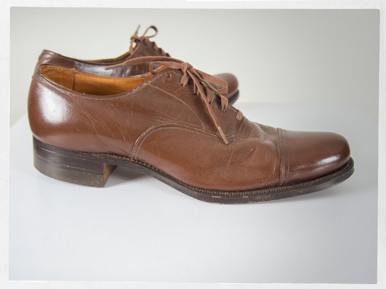 May include: A pair of brown leather lace-up shoes with a cap toe design. The shoes have a polished finish and are made of high-quality leather.