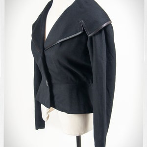 May include: A black cropped blazer with a wide collar and a single button closure. The collar has a black satin trim.