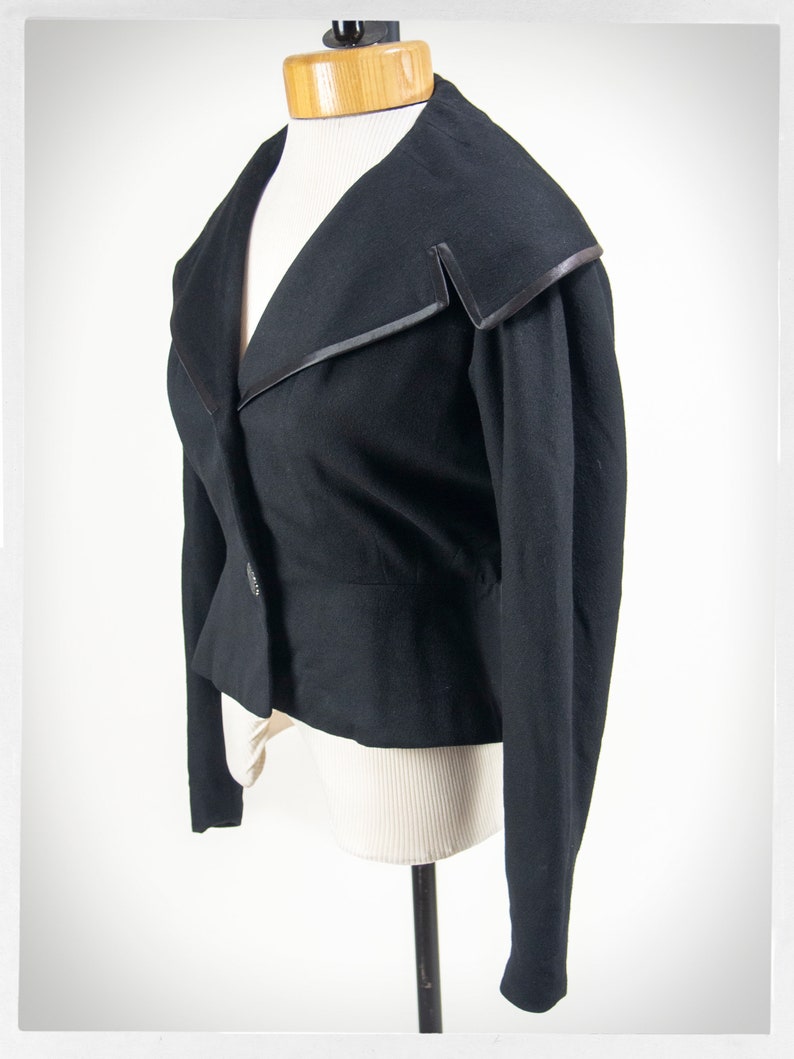 May include: A black cropped blazer with a wide collar and a single button closure. The collar has a black satin trim.