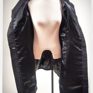 May include: A black coat with a satin lining. The coat is open and hanging on a mannequin.