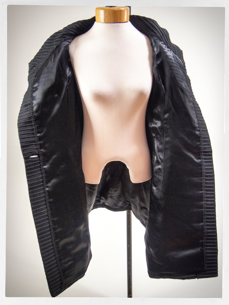 May include: A black coat with a satin lining. The coat is open and hanging on a mannequin.