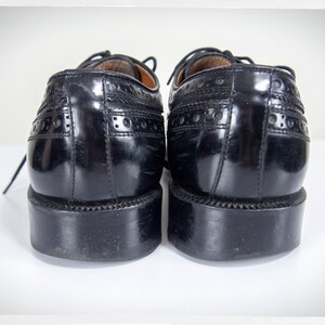 Op de afbeelding: Een paar zwarte leren schoenen met brogue details. De schoenen hebben een vetersluiting en een ronde neus.