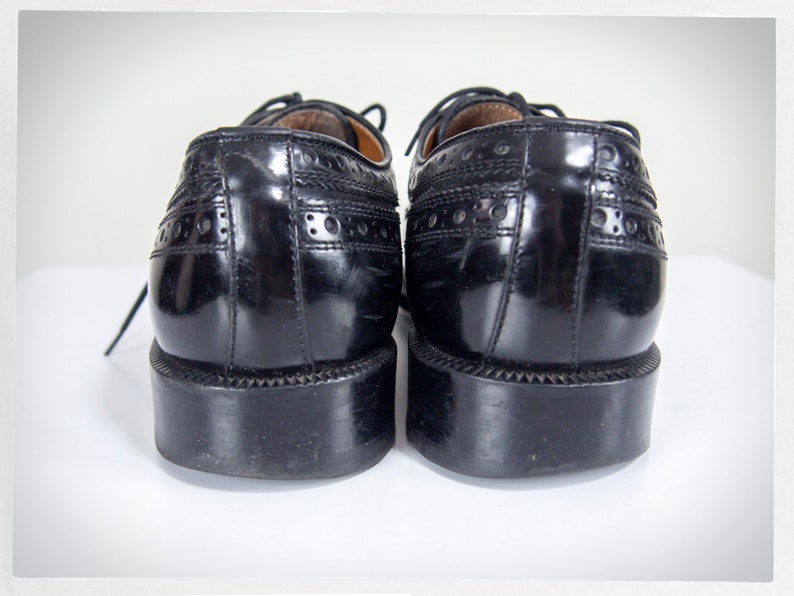 Op de afbeelding: Een paar zwarte leren schoenen met brogue details. De schoenen hebben een vetersluiting en een ronde neus.