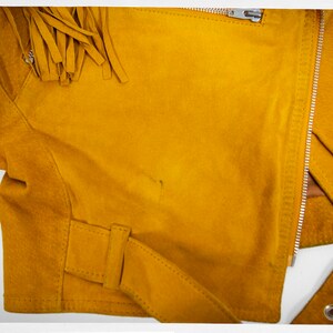 May include: A mustard yellow suede jacket with fringe detail on the shoulders and a zipper closure.