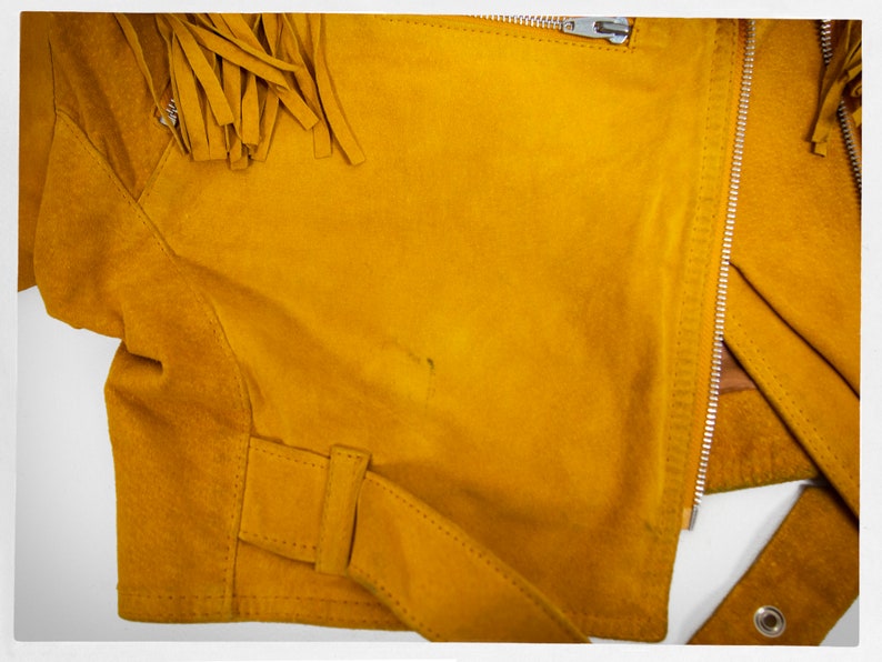 May include: A mustard yellow suede jacket with fringe detail on the shoulders and a zipper closure.