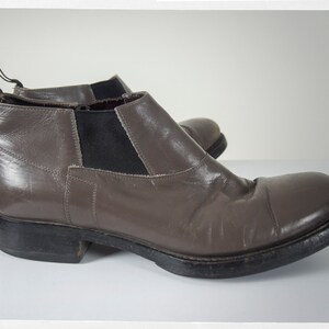 May include: A pair of brown leather ankle boots with a black elastic panel on the side. The boots have a rounded toe and a thick black sole.