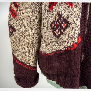 May include: A brown, cream, and red knitted cardigan with a zipper closure. The cardigan has a fair isle pattern and a brown ribbed knit collar, cuffs, and hem.