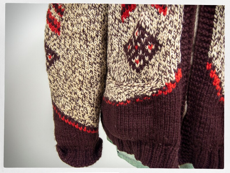 May include: A brown, cream, and red knitted cardigan with a zipper closure. The cardigan has a fair isle pattern and a brown ribbed knit collar, cuffs, and hem.
