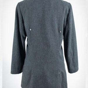 May include: A dark gray blazer with long sleeves, viewed from the back. The blazer has a notched collar and three small buttons on the back. The blazer is displayed on a mannequin, with blue jeans visible at the bottom.