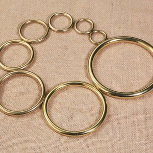 May include: A set of eight gold-colored metal rings of varying sizes, arranged in a circle on a brown fabric background.