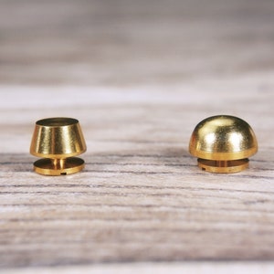 May include: Two gold-colored metal furniture knobs. One knob is round and the other is cone-shaped.