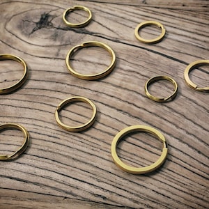 Pode incluir: Um conjunto de oito argolas de chave douradas de tamanhos diferentes, dispostas sobre uma superfície de madeira.